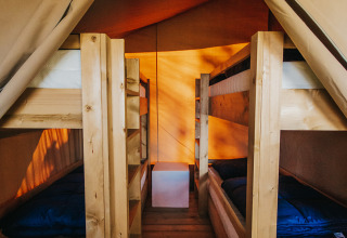 Interno di tenda safari con quattro letti a castello in legno e pavimento in legno al Camping Lucherino, Italia.