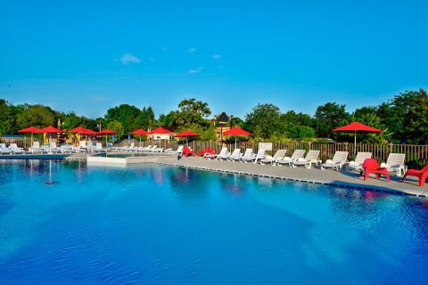 Outdoor swimming pool with white sun loungers and red umbrellas at Flower Camping L'Ile d'Offard, France.