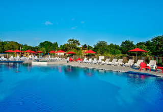 Outdoor swimming pool with white sun loungers and red umbrellas at Flower Camping L'Ile d'Offard, France.