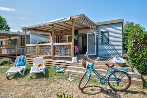 Cozy lodge with wooden deck, lounge chairs, bicycle, and garden, photographed on a sunny day.