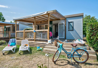 Confortevole lodge con veranda in legno, lettini, bicicletta e giardino in una giornata di sole.