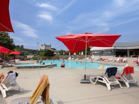 Outdoor swimming pool with red umbrellas, lounge chairs, and a castle view at Flower Camping L'Ile d'Offard, France.