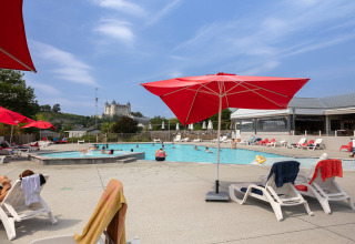 Piscine extérieure avec parasols rouges et vue sur un château, au Flower Camping L'Ile d'Offard, Pays de la Loire, France.