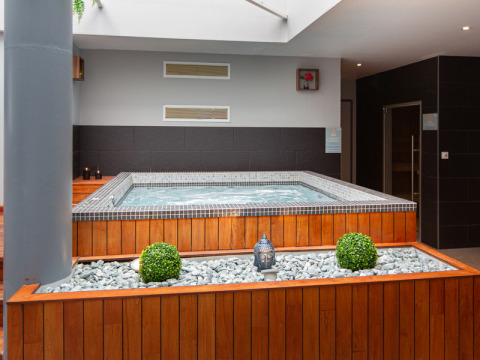 Indoor hot tub with wooden paneling, white decorative stones and plants at Flower Camping L'Ile d'Offard, France.