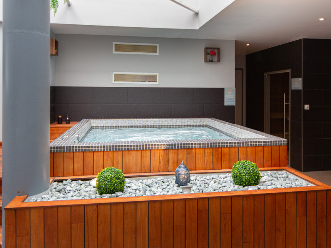 Jacuzzi interior con paneles de madera, piedras decorativas y plantas en Flower Camping L'Ile d'Offard, Francia.