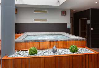 Jacuzzi interior con paneles de madera, piedras decorativas y plantas en Flower Camping L'Ile d'Offard, Francia.