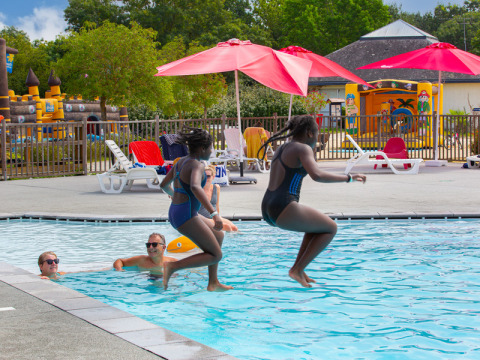 Deux enfants sautent dans la piscine au Flower Camping L'Ile d'Offard, entourés de transats et parasols rouges.