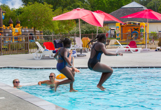 Deux enfants sautent dans la piscine au Flower Camping L'Ile d'Offard, entourés de transats et parasols rouges.