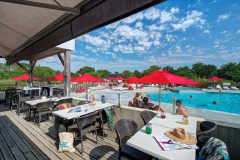 Buitenterras naast het zwembad met rode parasols bij Flower Camping L'Ile d'Offard in Pays de la Loire.