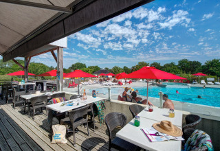 Outdoor terrace by the pool with red umbrellas and relaxed guests at Flower Camping L'Ile d'Offard, France.