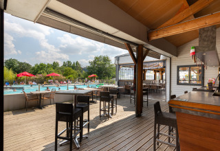 Terraza cubierta con bar y vista a la piscina y huéspedes en Flower Camping L'Ile d'Offard en Francia.
