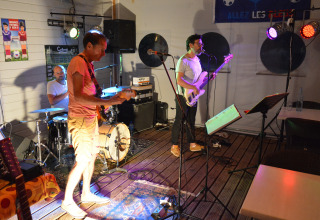 Et band optræder live på en lille scene med farvet belysning på Flower Camping L'Ile d'Offard i Frankrig.