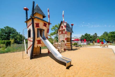 Playground with whimsical wooden towers and a slide at Flower Camping L'Ile d'Offard, Pays de la Loire, France.