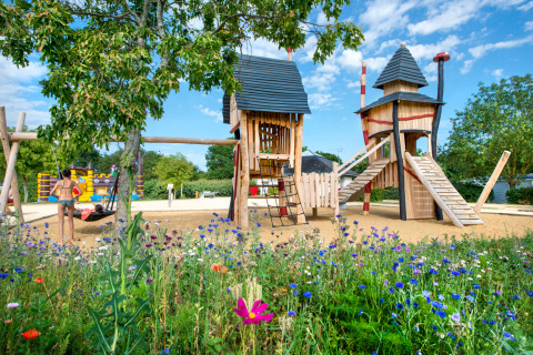 Speeltuin met fantasierijke houten torens en wilde bloemen bij Flower Camping L'Ile d'Offard in Frankrijk.