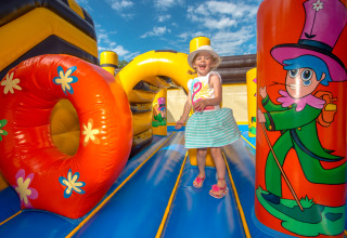 Niña feliz jugando en castillo hinchable colorido en Flower Camping L'Ile d'Offard, Pays de la Loire, Francia.