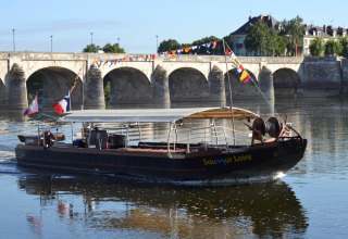 Boot fährt auf dem Fluss vor einer Steinbrücke bei Flower Camping L'Ile d'Offard in Pays de la Loire, Frankreich.