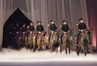 Reiter in Uniformen auf Pferden treten bei einer Indoor-Veranstaltung mit Nebel in Pays de la Loire, Frankreich auf.