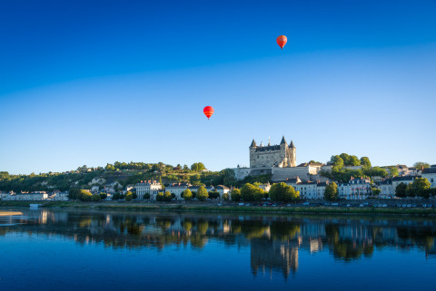 Vista de Flower Camping L'Ile d'Offard en Pays de la Loire con globos aerostáticos y castillo junto al río.