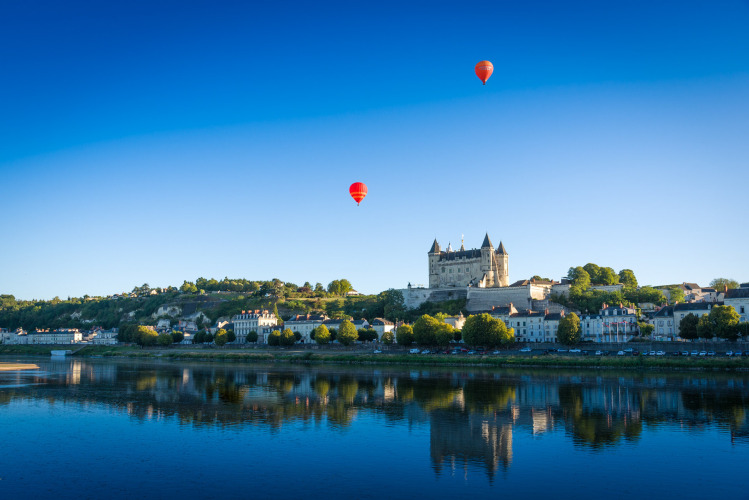 Vista de Flower Camping L'Ile d'Offard en Pays de la Loire con globos aerostáticos y castillo junto al río.