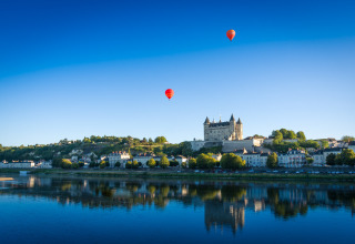 Vue de Flower Camping L'Ile d'Offard en Pays de la Loire avec des montgolfières et un château au bord de l’eau.