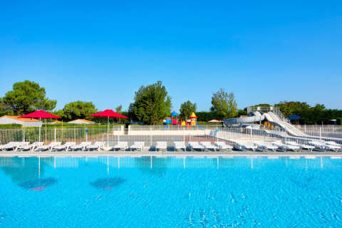 Piscina al aire libre con tumbonas, sombrillas rojas y toboganes de agua en Flower Camping Les Ilates, Francia.