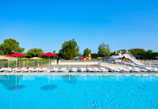 Piscine extérieure avec transats, parasols rouges et toboggans aquatiques au Flower Camping Les Ilates, France.