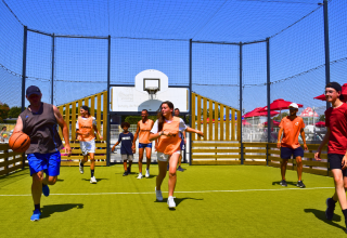 Grupo de personas juega baloncesto al aire libre en Flower Camping Les Ilates, parque vacacional en Nouvelle-Aquitaine.