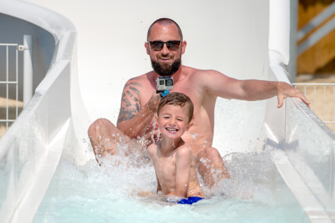 Padre e figlio si divertono sullo scivolo d'acqua al Flower Camping Les Ilates, Nouvelle-Aquitaine, Francia.