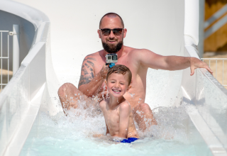 Padre e figlio si divertono sullo scivolo d'acqua al Flower Camping Les Ilates, Nouvelle-Aquitaine, Francia.