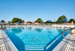 Großer Pool mit Liegestühlen und bunten Sonnenschirmen im Flower Camping Les Ilates, Nouvelle-Aquitaine, Frankreich.