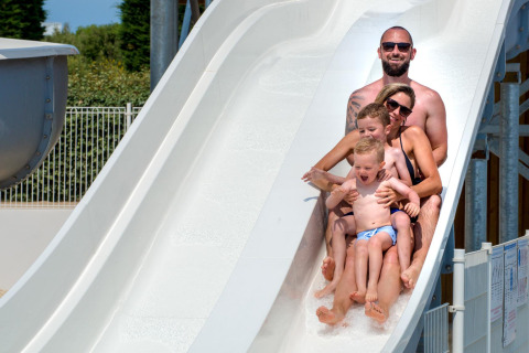 Una familia de cuatro baja sonriente por un gran tobogán de agua blanca en un parque vacacional en Francia.
