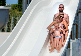 Une famille de quatre personnes s’amuse en descendant un grand toboggan aquatique blanc dans un camping en France.