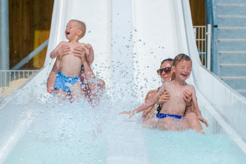 Twee volwassenen en twee kinderen lachen terwijl ze van de waterglijbaan gaan bij Flower Camping Les Ilates.