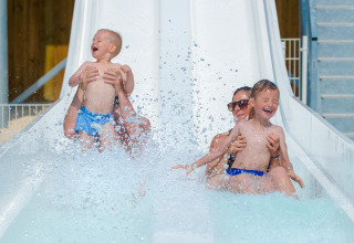 Due adulti e due bambini ridono felici mentre scendono dallo scivolo d'acqua al Flower Camping Les Ilates.