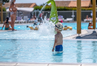 Un niño con sombrero está en la piscina de Flower Camping Les Ilates en Nouvelle-Aquitaine, Francia.