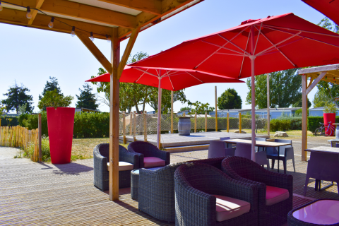 Buitenterras in de buurt van Loix, Frankrijk, met rieten stoelen en opvallende rode parasols onder een pergola.
