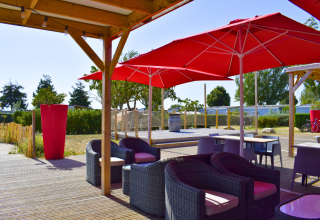 Terrasse extérieure près de Loix, France, avec des fauteuils en rotin et des parasols rouges sous une pergola.