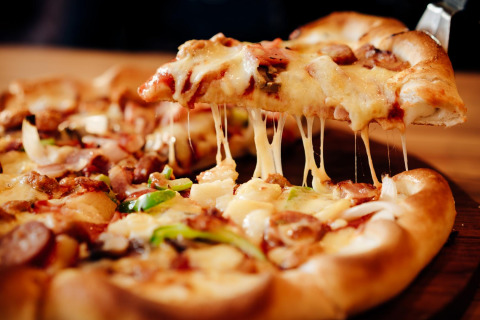 A close-up of a delicious, cheesy pizza slice being lifted from a freshly baked pizza on a wooden table.