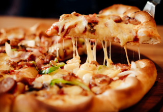 Een smakelijk stukje pizza met smeltende kaas wordt uit een versgebakken pizza op een houten tafel getild.