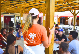 Young people gather around a table under a wooden canopy at Flower Camping Les Ilates in Nouvelle-Aquitaine, France.