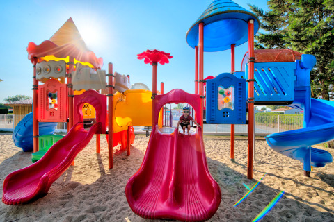 Parco giochi colorato con scivoli e sabbia, bambini che giocano al sole al Flower Camping Les Ilates.