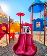 Kleurrijke speeltuin met glijbanen en zand, kinderen spelen in de zon bij Flower Camping Les Ilates.
