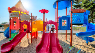 Bunter Spielplatz mit Rutschen und Sand, Kinder spielen in der Sonne im Flower Camping Les Ilates.