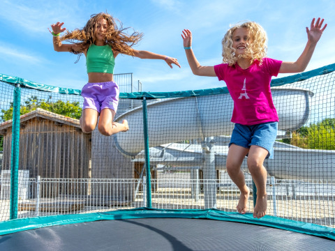 Twee kinderen amuseren zich op een outdoor trampoline bij Flower Camping Les Ilates in Nouvelle-Aquitaine, Frankrijk.