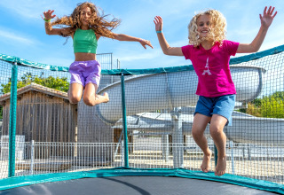 Zwei Kinder springen fröhlich auf einem Trampolin im Freien bei Flower Camping Les Ilates, Frankreich.