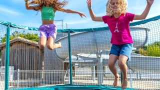 Zwei Kinder springen fröhlich auf einem Trampolin im Freien bei Flower Camping Les Ilates, Frankreich.