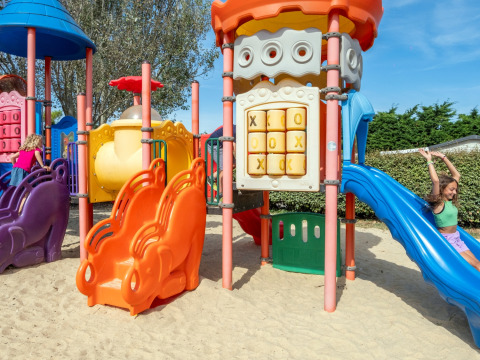 Kinder spielen auf einem bunten Spielplatz mit Rutschen im Sand im Flower Camping Les Ilates, Frankreich.