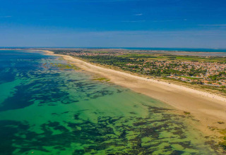 Luchtfoto van een vakantiepark met glamping aan een lang zandstrand en helder zeewater onder blauwe lucht.