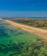 Luftaufnahme eines Ferienparks mit Glamping-Unterkünften an einem langen Sandstrand und klarem Meer.