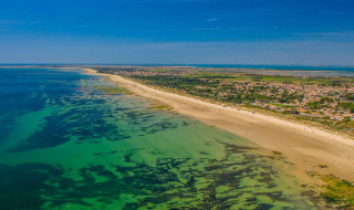 Vue aérienne d’un parc de vacances avec hébergements glamping, plage de sable et eau claire sous ciel bleu.